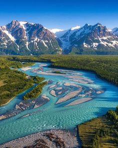 an aerial view of a river running through a valley surrounded by snow capped mountains in the distance