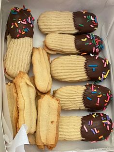 a box filled with lots of cookies covered in chocolate frosting and sprinkles