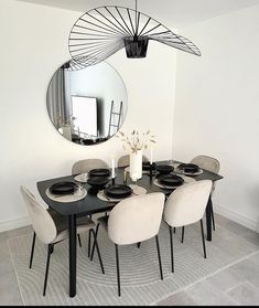 a dining room table with chairs and a round mirror on the wall above it,