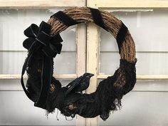 a black bird sitting on top of a wreath in front of a window sill