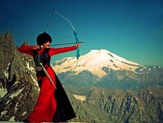 a woman in red dress holding an arrow on top of a snow covered mountain