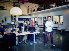 a man is standing in an office with his arms crossed and other people are sitting at desks