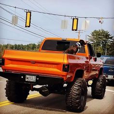 an orange truck driving down the road with a dog sticking its head out the window