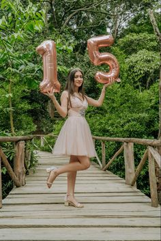 a woman in a short dress is holding two large balloons and posing on a bridge