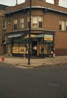 an old brick building with two men standing in the doorway and on the street corner