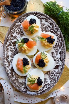 deviled eggs topped with smoked salmon and black cavia on a brown and white plate