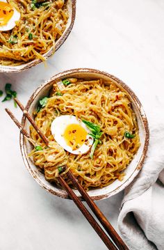 two bowls filled with noodles and eggs on top of a white tablecloth next to chopsticks