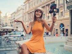 a woman in an orange dress is holding a video camera and posing for the camera