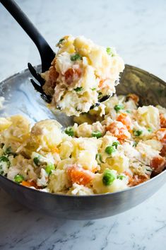 a spoon full of mashed potatoes with peas and carrots in it on a marble surface