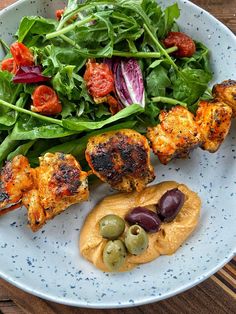 a white plate topped with meat and vegetables on top of a wooden table next to a salad