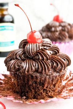 two cupcakes with chocolate frosting and cherries on top