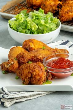 fried chicken with lettuce and ketchup on a white platter next to bowls of salad