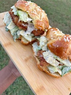 two sandwiches with meat, cheese and lettuce are on a wooden cutting board