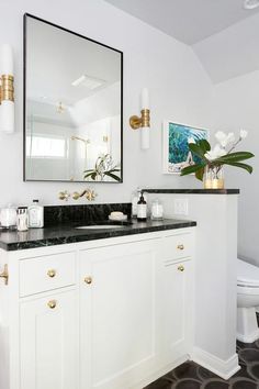 a white bathroom with black counter tops and gold accents on the mirror over the sink