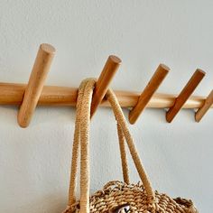 a straw bag hanging on a wooden coat rack with three pegs attached to it