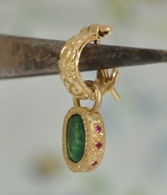 "A unique single earring on hanging on a hoop earring. 18k yellow gold oval pendant with oval green Emerald stone and 7 small Ruby stones set aside. A handmade unique gold bezel that I made especially for this green oval Emerald. On the side of the bezel, I set 7 red Ruby that makes this pendant even more beautiful and special. The oval emerald is set in a unique setting with gold dote all around. The Small Ruby stones on the side of the charm. The 18k gold oval bezel is hanging on a small gold Single Emerald Earring In Yellow Gold, Oval Emerald Earrings In Yellow Gold, Yellow Gold Oval Emerald Earrings, Oval Yellow Gold Emerald Earrings, Fine Jewelry Single Oval Earring, Single Oval Yellow Gold Earring, Yellow Gold Oval-shaped Earrings Gift, Yellow Gold Oval Pendant Earrings For Gift, Yellow Gold Oval Earrings For Gifts