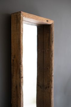 a wooden mirror hanging on the wall in front of a gray wall with a window