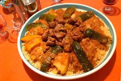 a bowl filled with meat and veggies on top of rice next to wine glasses