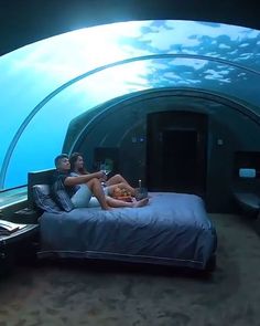 two people are sitting on a bed in an underwater bedroom with a view of the ocean