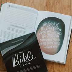 an open bible on a wooden table next to it's book titled the bible in a year