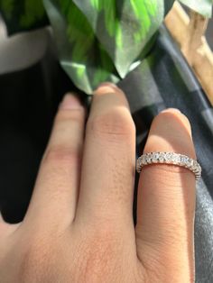 a person's hand with a diamond ring on their finger next to a plant