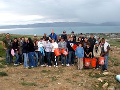 a group of people standing next to each other on top of a dirt field near the ocean