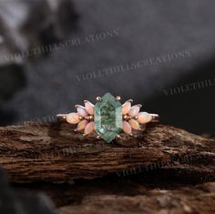 a ring with an emerald stone surrounded by peach and white flowers on top of a piece of wood