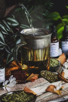 tea being poured into a glass pitcher with herbs and spices around it on a table