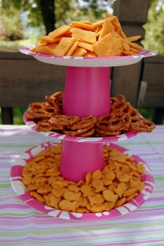 three tiered trays filled with snacks on top of a pink tablecloth covered picnic table