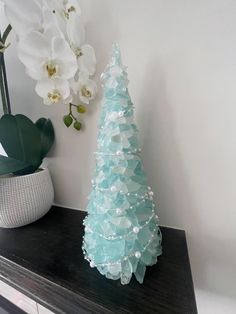 a glass christmas tree sitting on top of a wooden table next to a potted plant