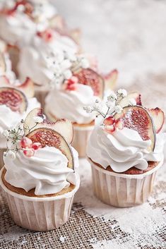 some cupcakes with white frosting and fruit on top are sitting on a table