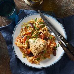 a white plate topped with pasta and meat next to a glass of wine on top of a table