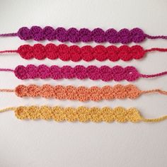 four crocheted bracelets are lined up on a white surface, one is pink, the other is yellow