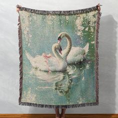 two white swans swimming in the water on a green and blue blanket with fringes