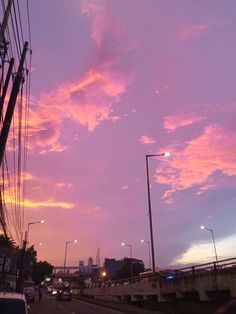 the sky is pink and purple as cars drive down the road