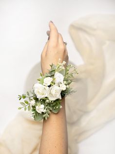 a woman's hand holding a bouquet of white flowers and greenery on her wrist