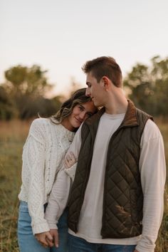 a young man and woman standing together in the grass with their arms around each other