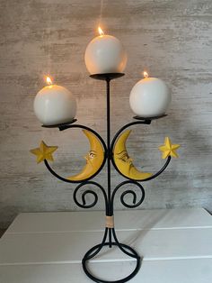 a candle holder with three candles on top of it and two stars hanging from the bottom