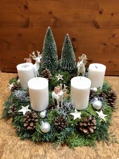 a christmas centerpiece with white candles and pine cones on the table next to it