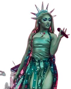 a woman dressed as the statue of liberty is holding a microphone in one hand and wearing a green dress