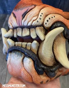 a close up of a person's hand holding a fake animal head with teeth