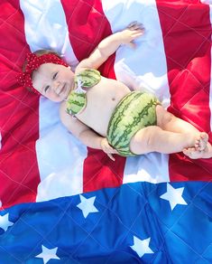 a baby in a watermelon suit laying on top of an american flag blanket