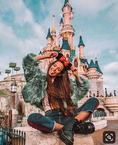 a woman sitting on the ground in front of a castle wearing a minnie mouse ears hat