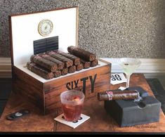 a wooden box filled with lots of cigars next to a cocktail glass and clock