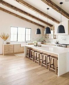 a large kitchen with an island and bar stools in the center, along with two black pendant lights hanging from the ceiling