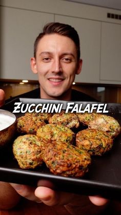 a man holding a tray full of food and dipping sauce in his hand with the caption zucchini falafel