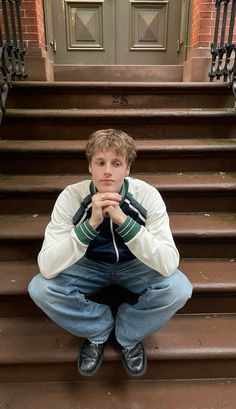 a young man is sitting on the steps with his hands folded in front of his face