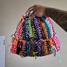 a hand holding a multicolored crocheted bag with string attached to it