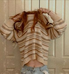 a woman standing in front of a door with her back to the camera, wearing ripped jeans and a striped sweater