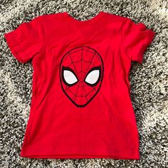 a red t - shirt with a spiderman face on it sitting on the carpet